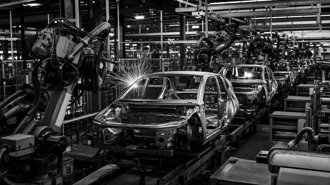Schwarz-Weiß-Industrieaufnahme einer modernen Elektrofahrzeug-Montagelinie mit Schweißrobotern, Funk