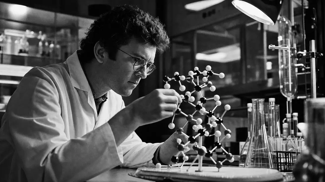 Schwarz-Weiß-Dokumentarfotografie eines Wissenschaftlers, der ein Molekülmodell im Pharmalabor untersucht, mit Filmkorn und dramatischem Kontrast