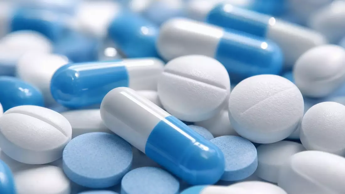 Extreme Makrofotografie generischer blauer und weißer Pharmatabletten und Kapseln ohne Aufschrift mit geringer Schärfentiefe auf klinischem Hintergrund