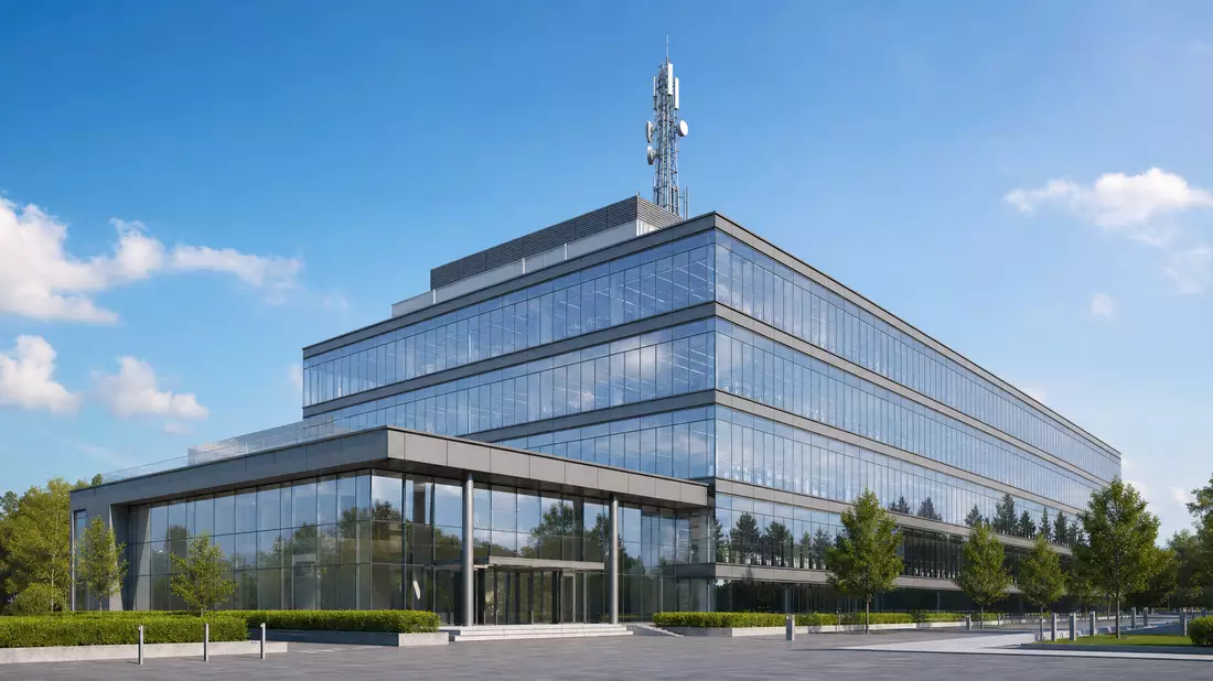 Modernes Glasbürogebäude mit Kommunikationsantenne auf dem Dach vor blauem Himmel