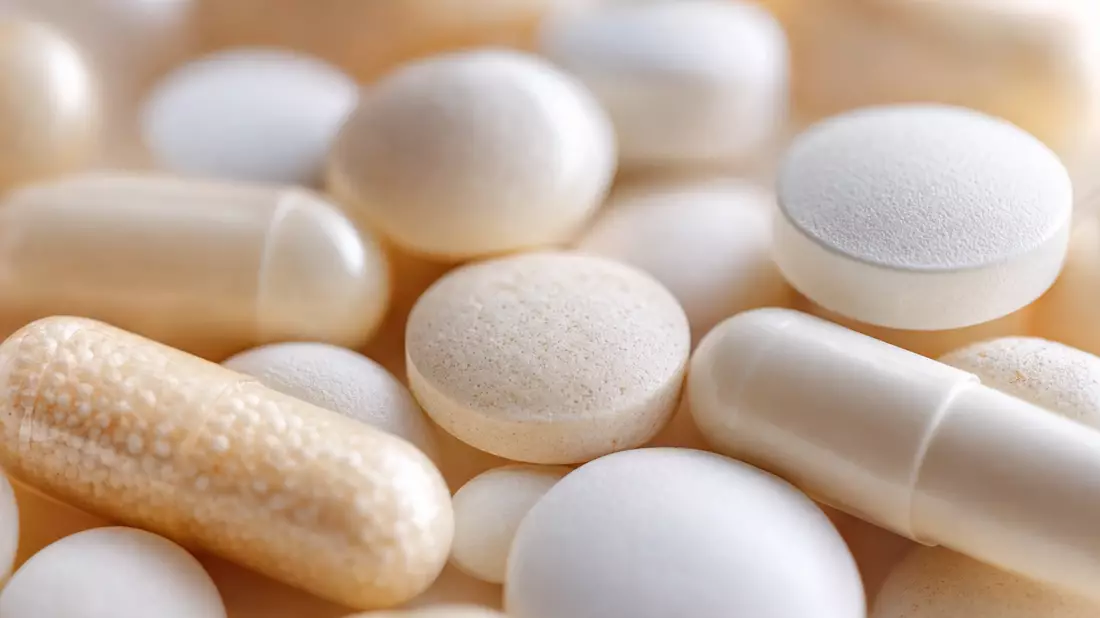 Extreme Makroaufnahme von unbeschrifteten Pharmakapseln und weißen Tabletten mit weichem Bokeh-Hintergrund, warmes klinisches Licht betont Oberflächentexturen