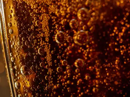 PepsiCo US7134481081 in extremer Makroaufnahme von Kohlensäureblasen in bernsteinfarbenem generischem Getränk ohne Logo - Foto: THN