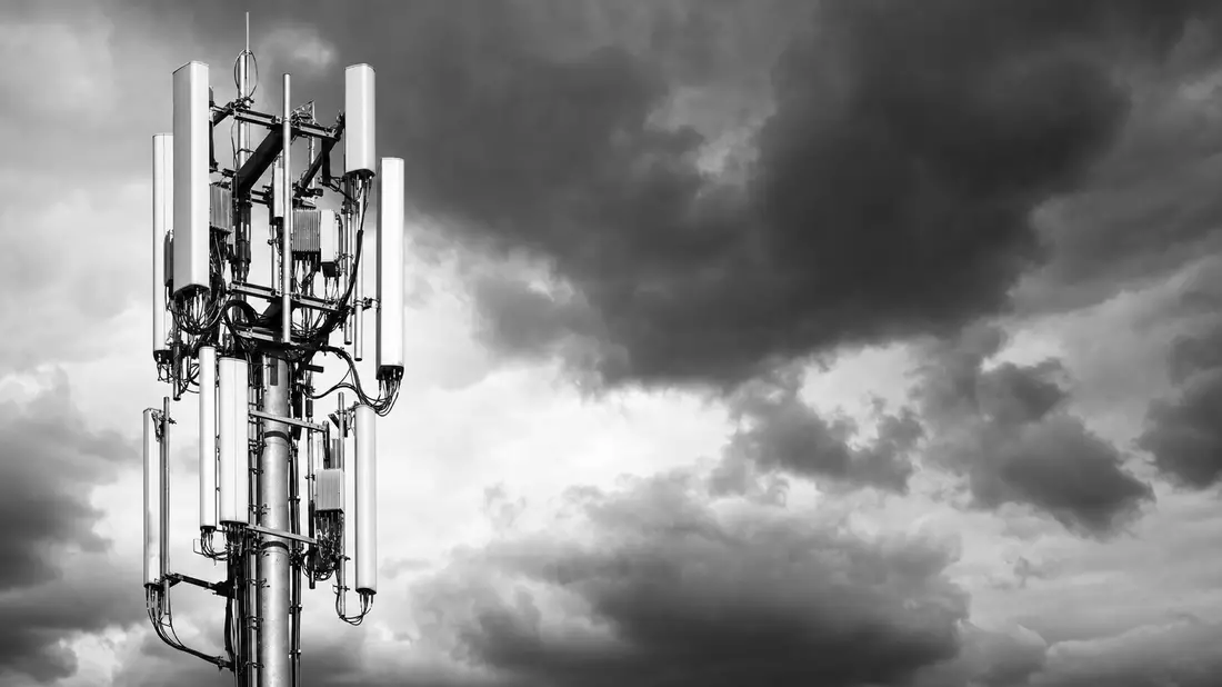 Schwarz-Weiß-Reportagefoto eines 5G-Antennenturms mit mehreren Panel-Antennen vor dramatisch bewölktem Himmel im Hochkontrast-Dokumentarstil