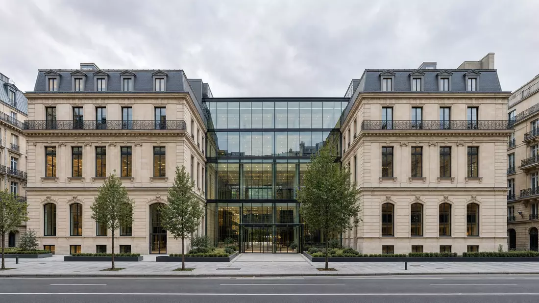 Architekturfoto eines symmetrischen Pariser Unternehmensgebäudes im Haussmann-Stil mit moderner Glasfront, breite Straßenperspektive, bewölkter Himmel