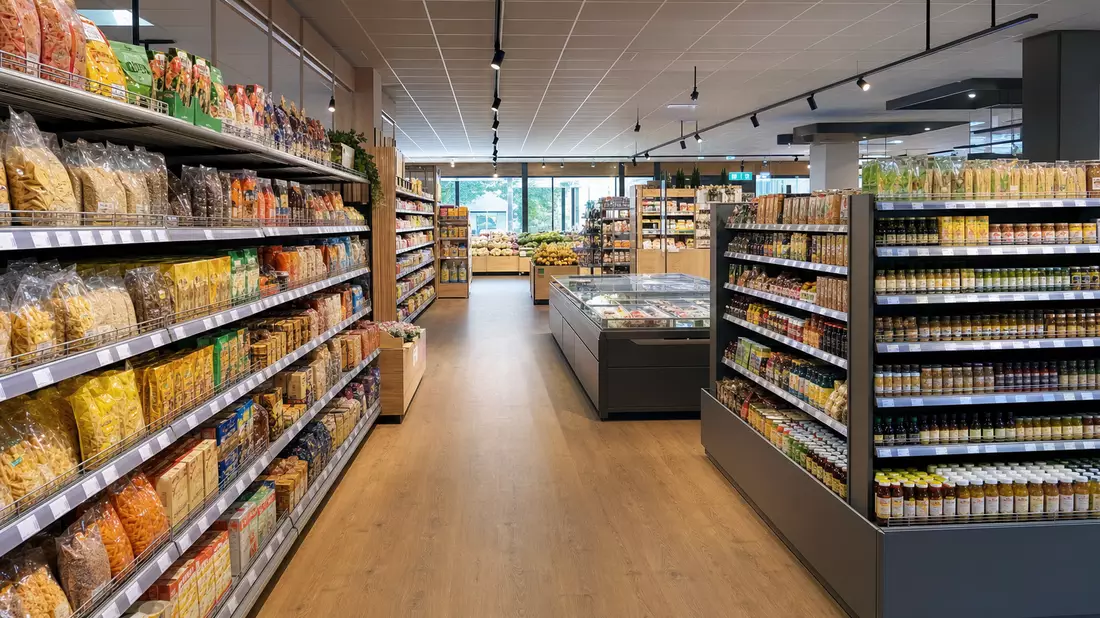 Fotorealistischer Blick in einen generischen europäischen Supermarkt mit hellen LED-beleuchteten Gängen, vollständig bestückten Regalen und einem warmen Holzboden – typischer niederländischer Lebensmitteleinzelhandel