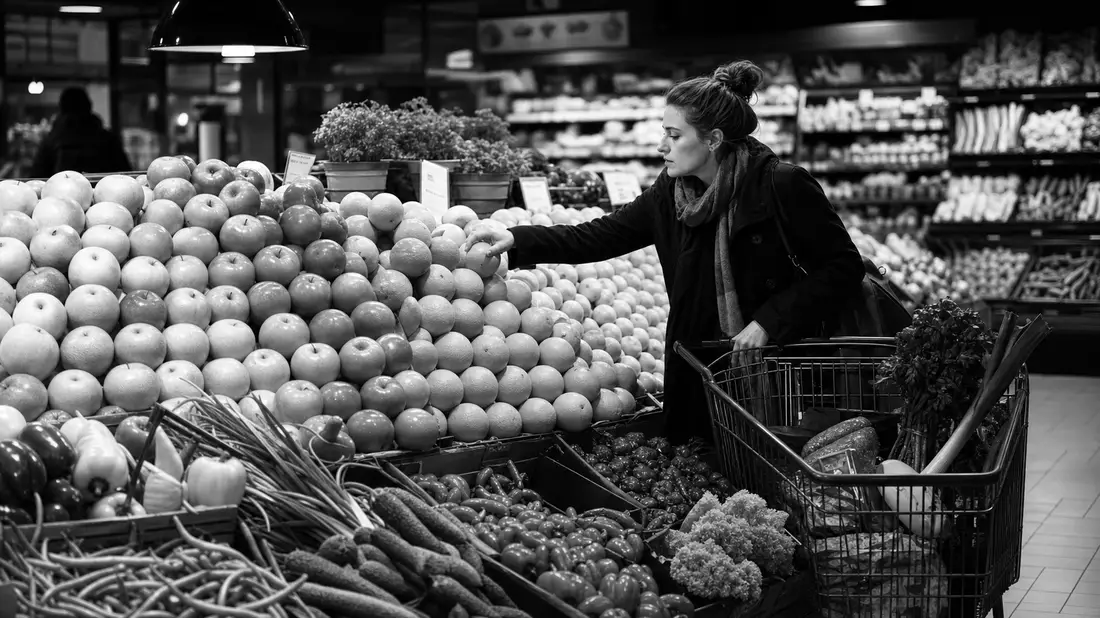 Schwarz-Weiß-Reportage aus der Obst- und Gemüseabteilung: Eine Frau greift in einer dramatisch belic