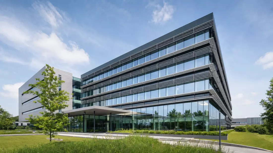 Architekturfotografie eines modernen Verwaltungsgebäudes in Zaandam, Niederlande – Glas-Stahl-Fassade mit horizontalen Sonnenschutzlamellen vor blauem Himmel und gepflegtem Grün