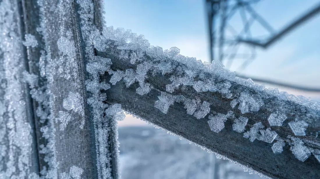 Extreme macro photo of intricate ice crystals and frost formations on steel high-voltage electricity pylon strut