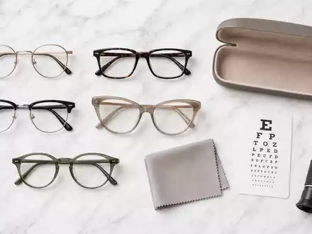EssilorLuxottica FR0000033219 flatlay of eyeglass frames, leather case, cleaning cloth, and refractometer on marble - Foto: THN
