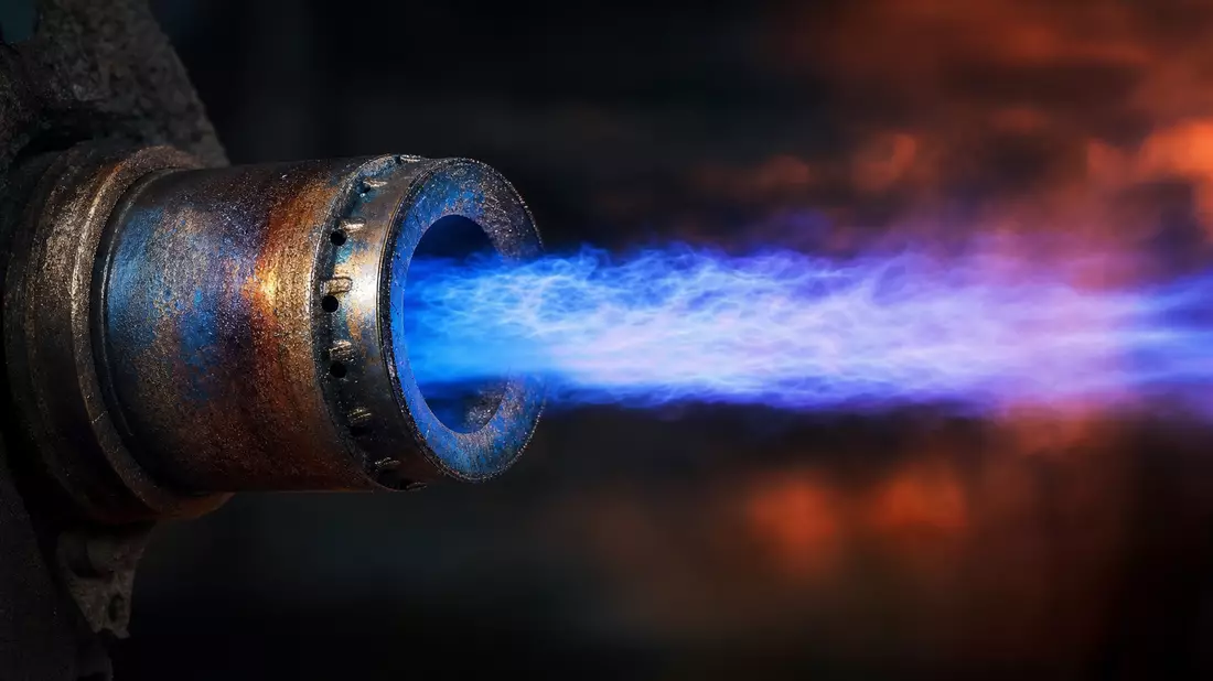 Macro close-up of industrial gas burner nozzle with intense blue flame in furnace
