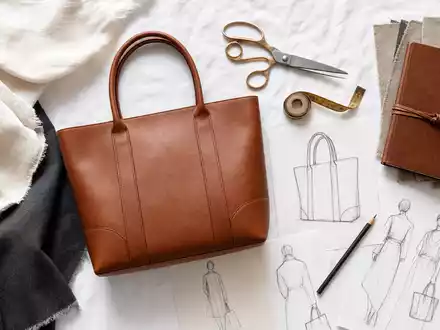 Kering FR0000121964 flatlay cognac leather tote bag fabric swatches scissors and fashion design sketches - Foto: THN