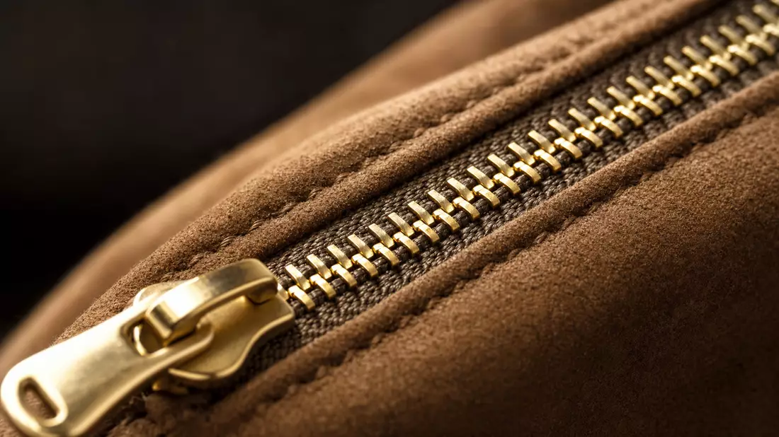 Extreme macro of gold metal zipper on dark champagne suede leather with shallow depth of field