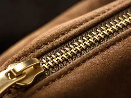 Kering FR0000121964 macro detail gold zipper on dark suede leather luxury craftsmanship shallow depth - Foto: THN