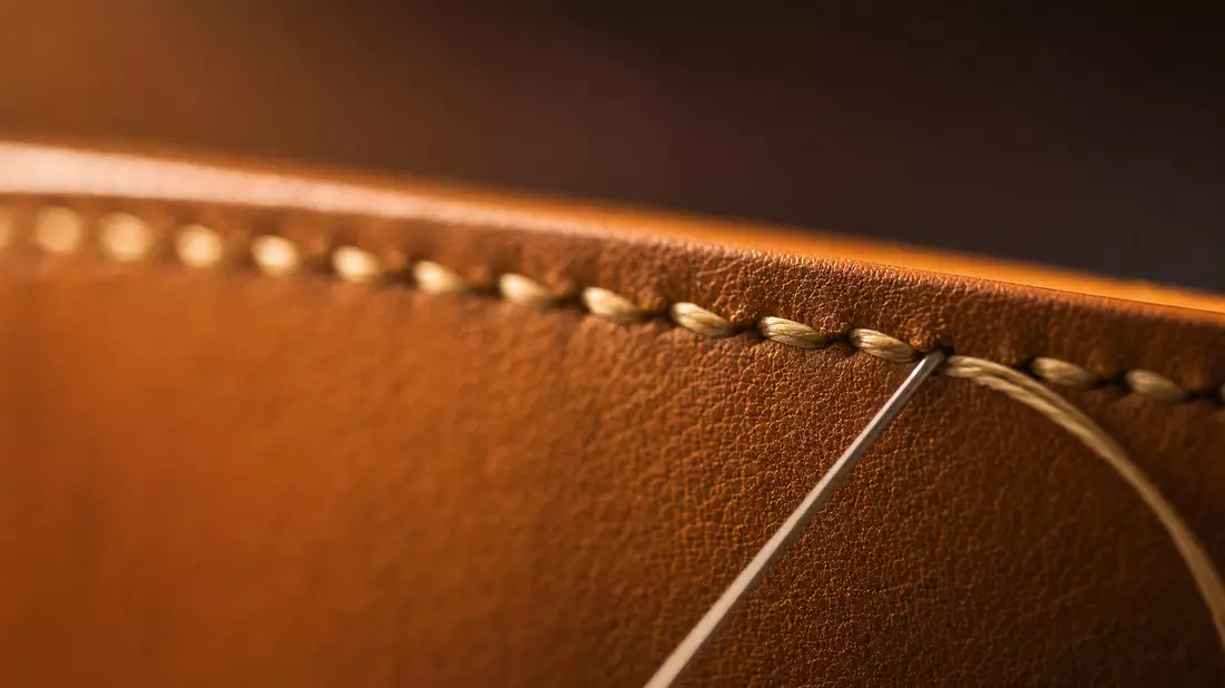 Extreme macro photo of hand-sewn cognac leather edge with precise waxed saddle stitch