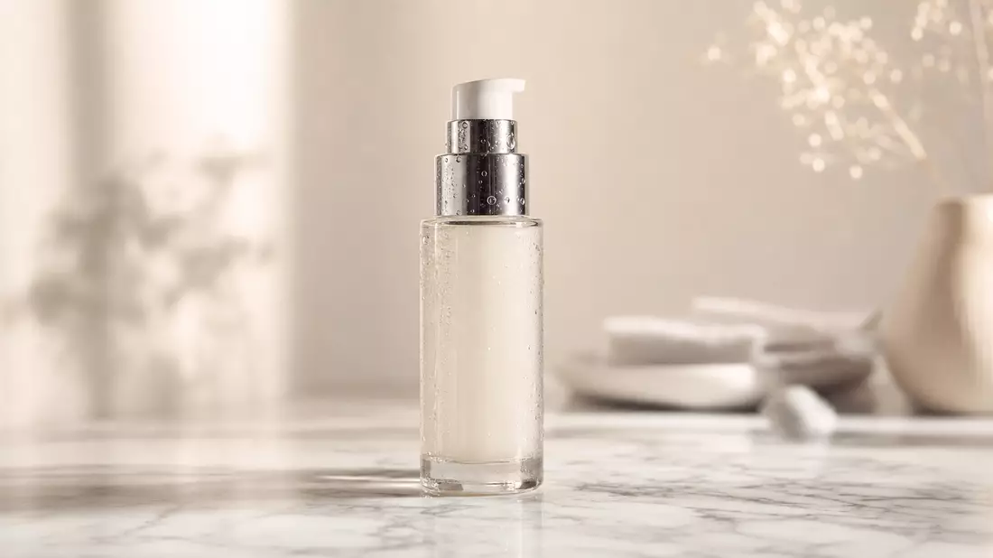 Unbranded glass cosmetic bottle with silver pump on white marble under soft studio lighting