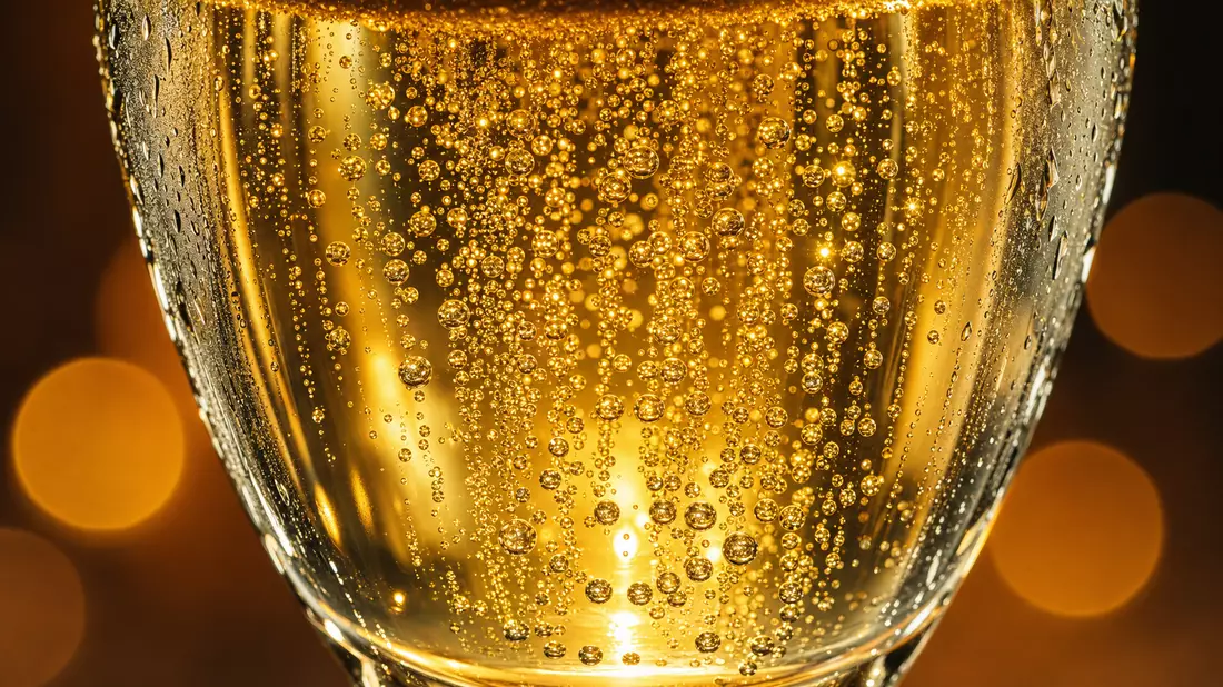 Extreme macro photo of golden champagne bubbles rising in crystal flute with bokeh light reflections