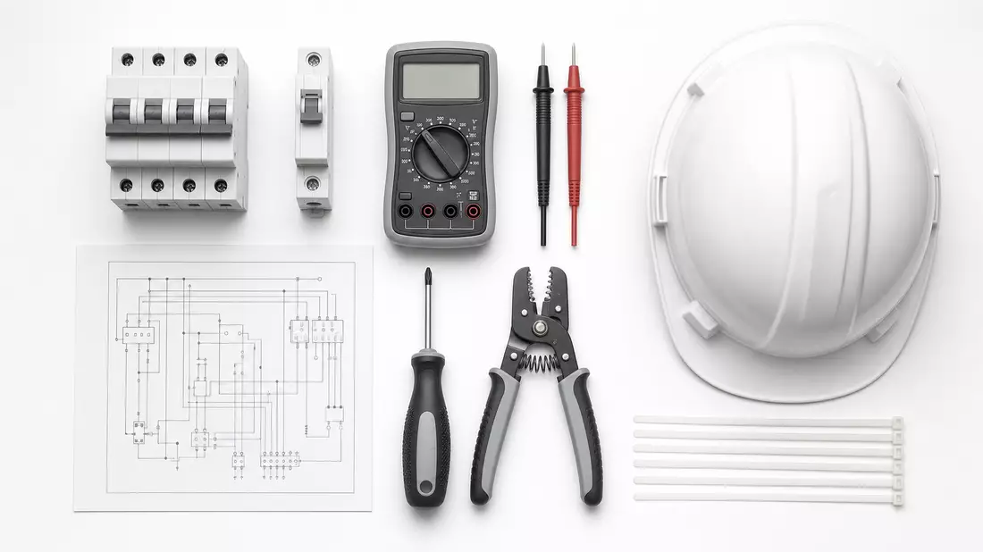 Overhead knolling flatlay of electrical components including circuit breakers, multimeter, wiring schematic, screwdriver and hard hat