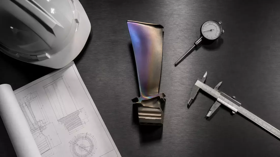 Flatlay of turbine blade, measuring tools, and engineering blueprint on dark surface