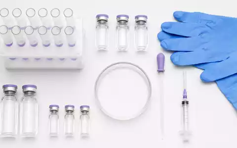 Sanofi FR0000120578 overhead flatlay of pharmaceutical vials, syringe, pipette, petri dish, and protective gloves - Foto: THN