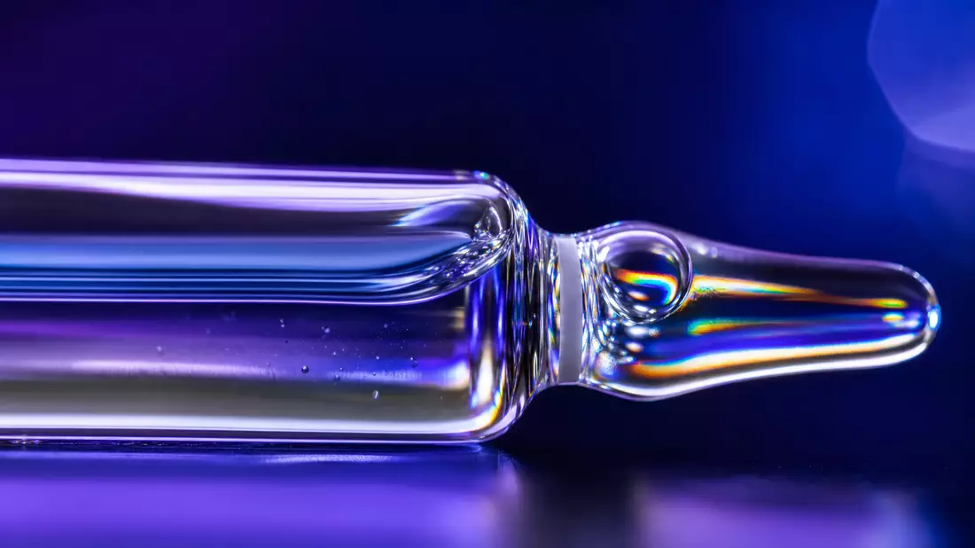 Extreme close-up macro photograph of a sealed glass pharmaceutical ampoule with brilliant caustic light reflections against a deep violet-blue background