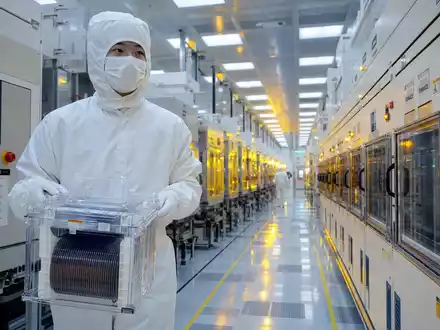 STMicroelectronics NL0000226223 cleanroom technician carries silicon wafer cassette under lithography safety lights - Foto: THN
