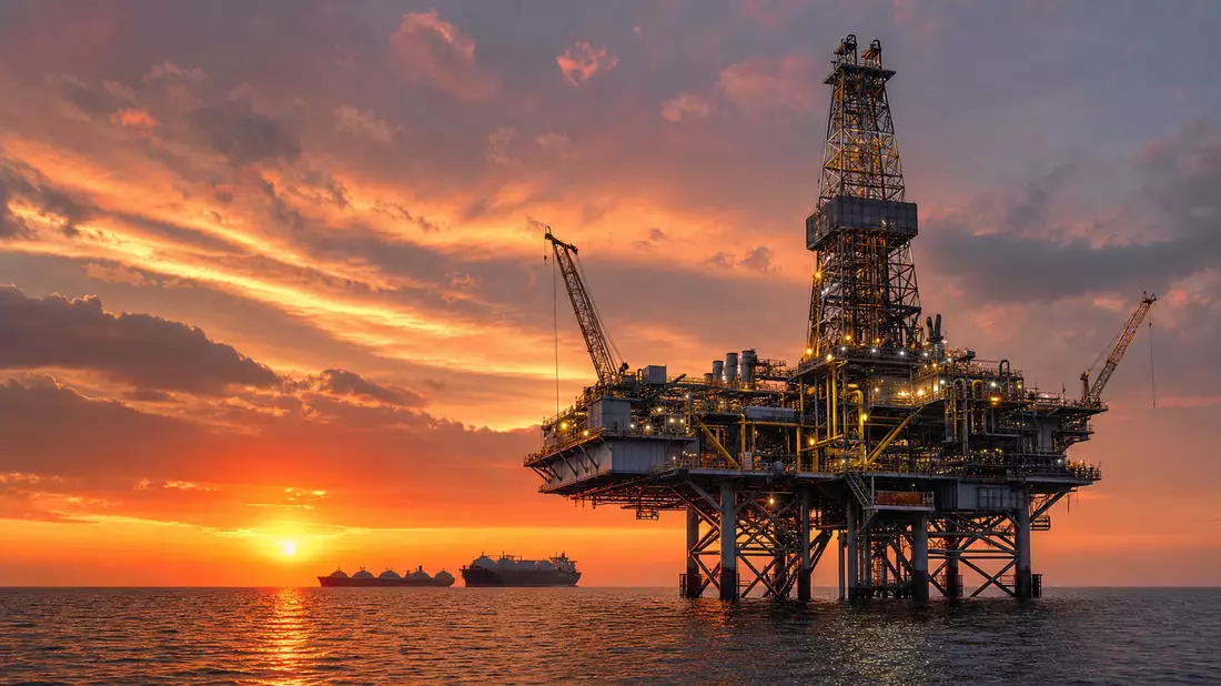 Offshore-Bohrplattform bei Sonnenuntergang, LNG-Tanker am Horizont über dem Meer