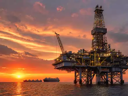 TotalEnergies FR0000120271 zeigt eine fotorealistische Offshore-Bohrplattform mit großen LNG-Tankern bei goldenem Meeressonnenuntergang - Foto: THN
