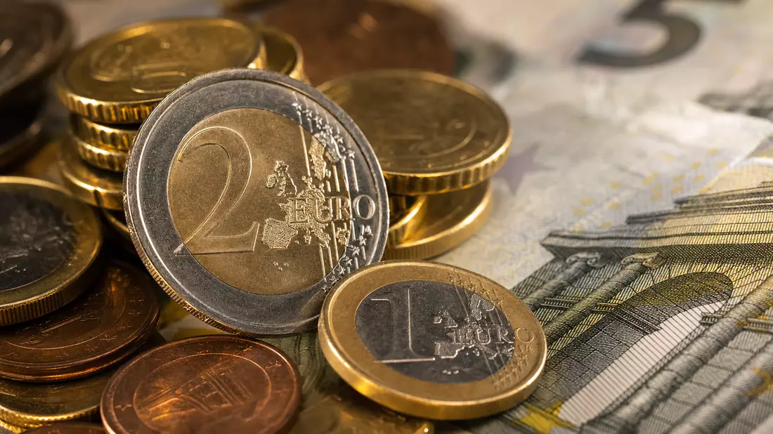 Makro-Fotografie gestapelter Euro-Münzen auf Banknoten mit warmem Bokeh-Hintergrund
