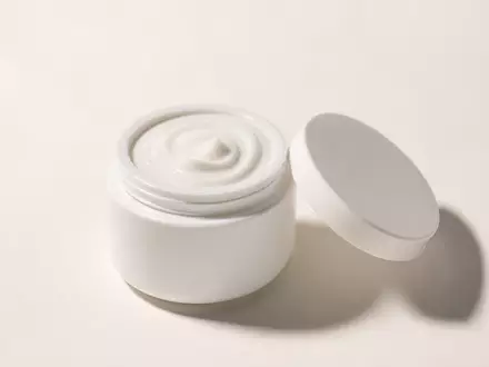 Fotorealistisches Studio-Produktbild einer geöffneten weißen, unbeschrifteten Keramik-Cremedose mit cremiger Textur, perlweißer Hintergrund, weiches Seitenlicht - Foto: THN
