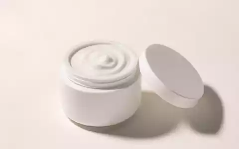 Fotorealistisches Studio-Produktbild einer geöffneten weißen, unbeschrifteten Keramik-Cremedose mit cremiger Textur, perlweißer Hintergrund, weiches Seitenlicht - Foto: THN