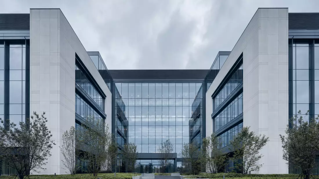 Moderner Unternehmens-Campus mit Glasfassade, symmetrische Architektur, bewölkter Himmel