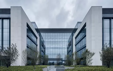 Architekturaufnahme eines modernen Unternehmens-Campus: symmetrische Fassade aus Glas und hellem Beton, nordeuropäisches Tageslicht, grüne Bepflanzung, kein Schriftzug - Foto: THN