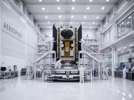 Airbus SE Raumfahrtsparte: Symmetrische Architekturfotografie eines Reinraumzentrums mit goldenem Satelliten auf Montageplattform, Schriftzug AEROSPACE - Foto: THN