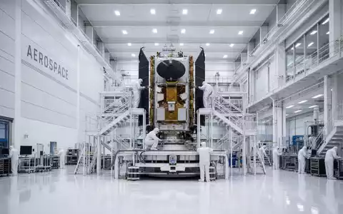 Airbus SE Raumfahrtsparte: Symmetrische Architekturfotografie eines Reinraumzentrums mit goldenem Satelliten auf Montageplattform, Schriftzug AEROSPACE - Foto: THN