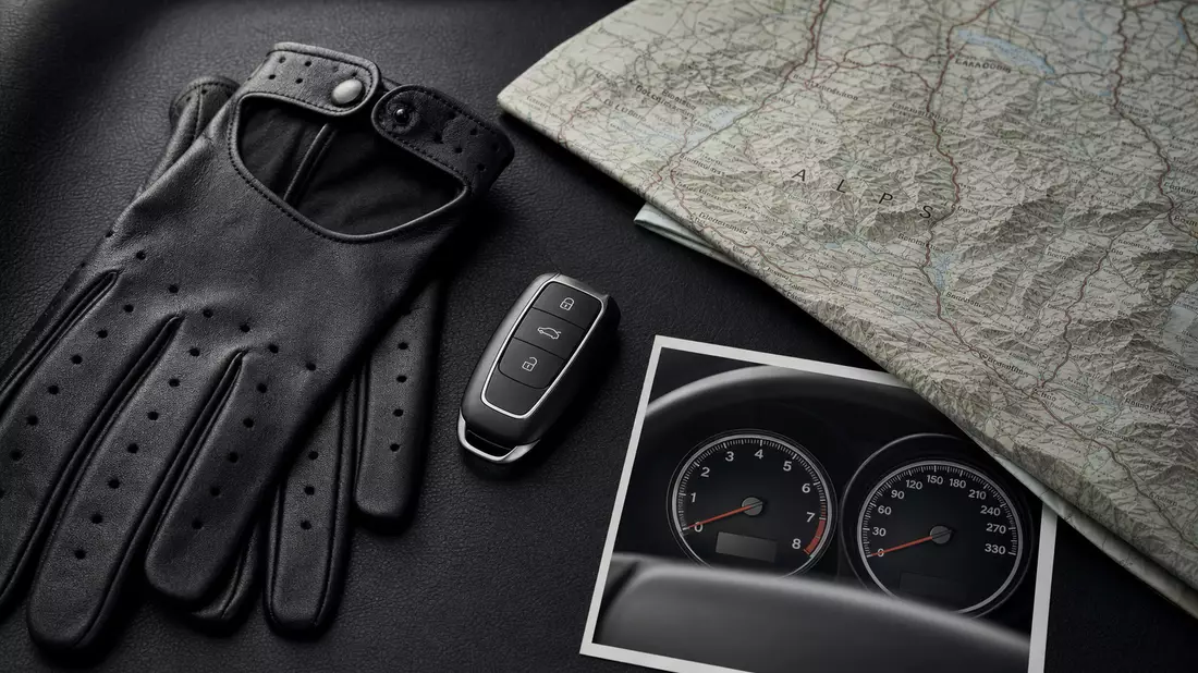 Flatlay Autoschlüssel, schwarze Lederhandschuhe, Alpenkarte, Tachometer-Bild auf Leder