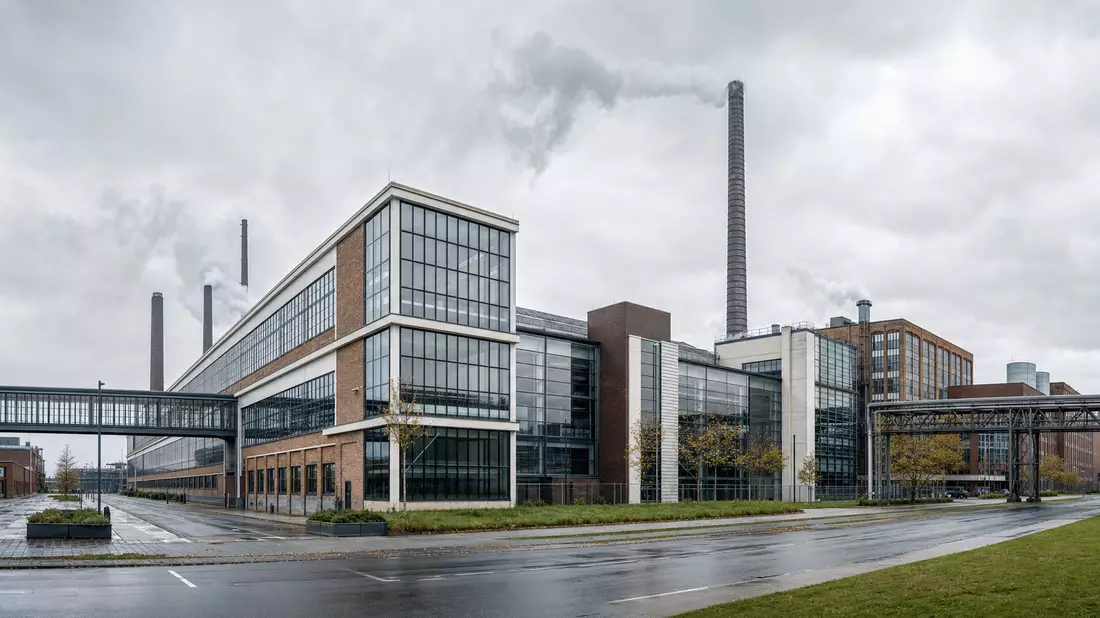 Modernes Industriegelände mit Schornsteinen, Backsteinfassade und Glasfronten unter bewölktem Himmel
