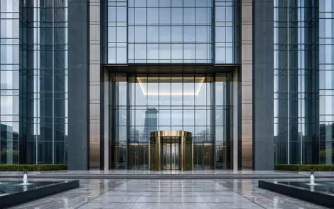 Architekturfotografie eines generischen Bankgebäudes für Commerzbank AG (ISIN DE000CBK1001). Glas-Stahl-Fassade mit Drehtür aus Messing, Brunnen im Vorplatz, präzise architektonische Linien - Foto: THN