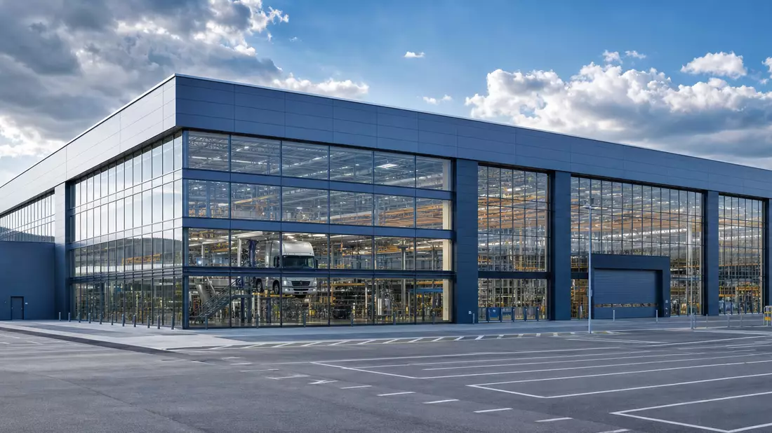 Modernes Nutzfahrzeugwerk mit gläserner Fassade und weitem Vorplatz unter bewölktem Himmel