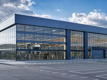 Architektonische Außenaufnahme einer modernen LKW-Endmontagehalle mit Stahl-Glas-Fassade im süddeutschen Industriestil – steht für den Standort der Daimler Truck Holding AG (ISIN DE000DTR0CK8) in Leinfelden-Echterdingen bei Stuttgart - Foto: THN