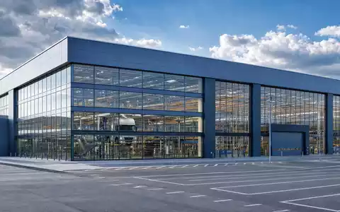 Architektonische Außenaufnahme einer modernen LKW-Endmontagehalle mit Stahl-Glas-Fassade im süddeutschen Industriestil – steht für den Standort der Daimler Truck Holding AG (ISIN DE000DTR0CK8) in Leinfelden-Echterdingen bei Stuttgart - Foto: THN