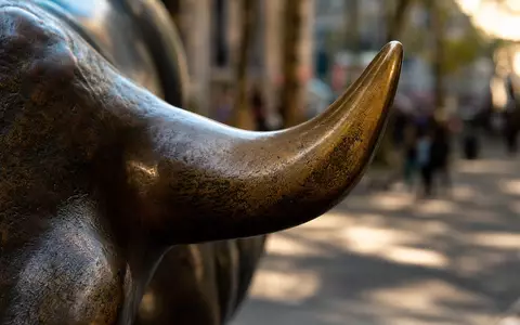 Makrofotografie für die Deutsche Börse AG (ISIN DE0005810055): Extremes Close-up einer Bronze-Bullenskulptur mit Fokus auf der Hornspitze, warme Patina-Textur, Bokeh-Hintergrund eines städtischen Platzes, dramatisches Seitenlicht - Foto: THN