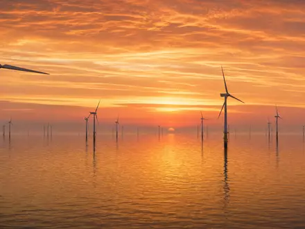 Fotorealistisches Panorama eines Offshore-Windparks in der Nordsee bei goldenem Sonnenuntergang. Zahlreiche weiße Windturbinen stehen im ruhigen Wasser, der orangefarbene Himmel spiegelt sich auf der glatten Meeresoberfläche. Dieses Bild steht exemplarisch für die Offshore-Windkraft-Aktivitäten von E.ON SE (ISIN DE000ENAG999) im Bereich erneuerbare Energien - Foto: THN