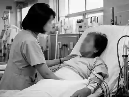 Eine eindringliche Schwarzweiß-Reportageaufnahme einer Pflegekraft beim Betreuen eines Patienten an einer Dialysemaschine – ein Motiv, das die menschliche Dimension der Dialyseversorgung wie bei Fresenius Medical Care AG (ISIN DE0005785802) verdeutlicht - Foto: THN