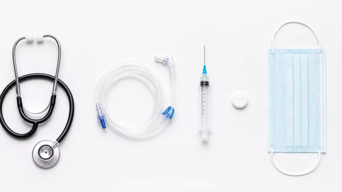 Flatlay medizinischer Utensilien: Stethoskop, Dialyseschlauch, Spritze, Tablette und Maske auf weißem Hintergrund
