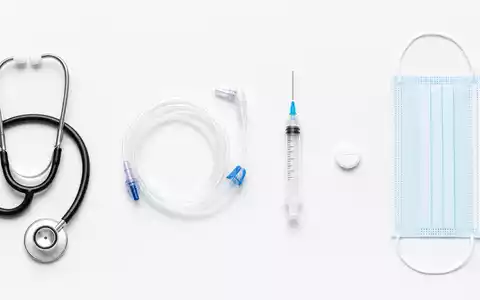 Eine Top-down-Flatlay-Aufnahme medizinischer Utensilien – Stethoskop, ungebrandeter Dialyseschlauch, Spritze, Tablette und Maske – als Symbolik für die medizintechnische Produktpalette der Fresenius Medical Care AG (ISIN DE0005785802) - Foto: THN