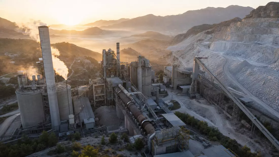 Industrielles Zementwerk mit Drehofen und Schornsteinen bei goldenem Sonnenaufgang