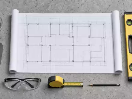 Flatlay-Draufsicht auf Bauplan, Zementprobe, Maurerkelle, Wasserwaage und Schutzbrille – Arbeitsmaterialien rund um die Kernprodukte der Heidelberg Materials AG (ISIN DE0006047004) - Foto: THN