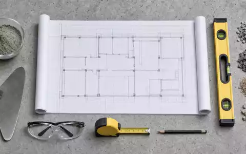 Flatlay-Draufsicht auf Bauplan, Zementprobe, Maurerkelle, Wasserwaage und Schutzbrille – Arbeitsmaterialien rund um die Kernprodukte der Heidelberg Materials AG (ISIN DE0006047004) - Foto: THN