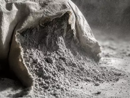 Makrofotografie eines geöffneten Zementsacks mit feinem Zementstaub in der Luft – das Kernprodukt der Heidelberg Materials AG (ISIN DE0006047004) in extremer Nahaufnahme - Foto: THN