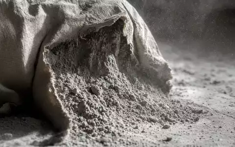 Makrofotografie eines geöffneten Zementsacks mit feinem Zementstaub in der Luft – das Kernprodukt der Heidelberg Materials AG (ISIN DE0006047004) in extremer Nahaufnahme - Foto: THN